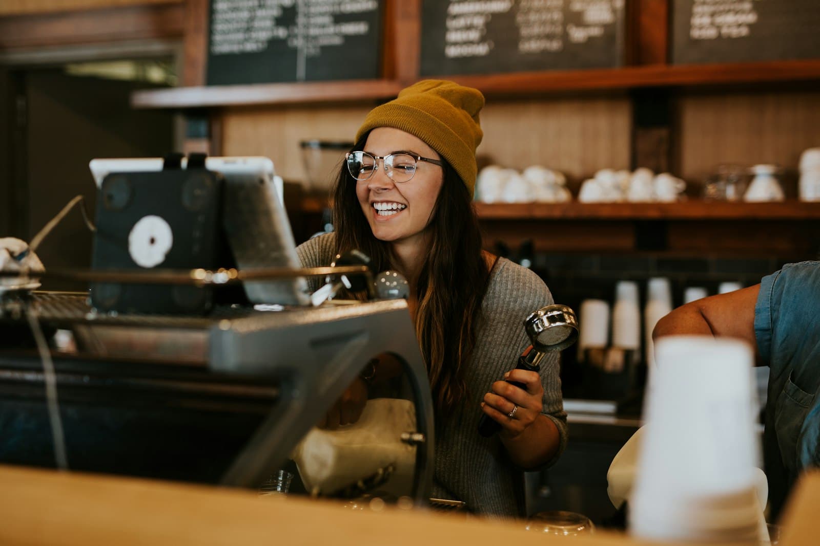 Una barista sonríe junto a la pantalla de cobro en el mostrador de una cafetería