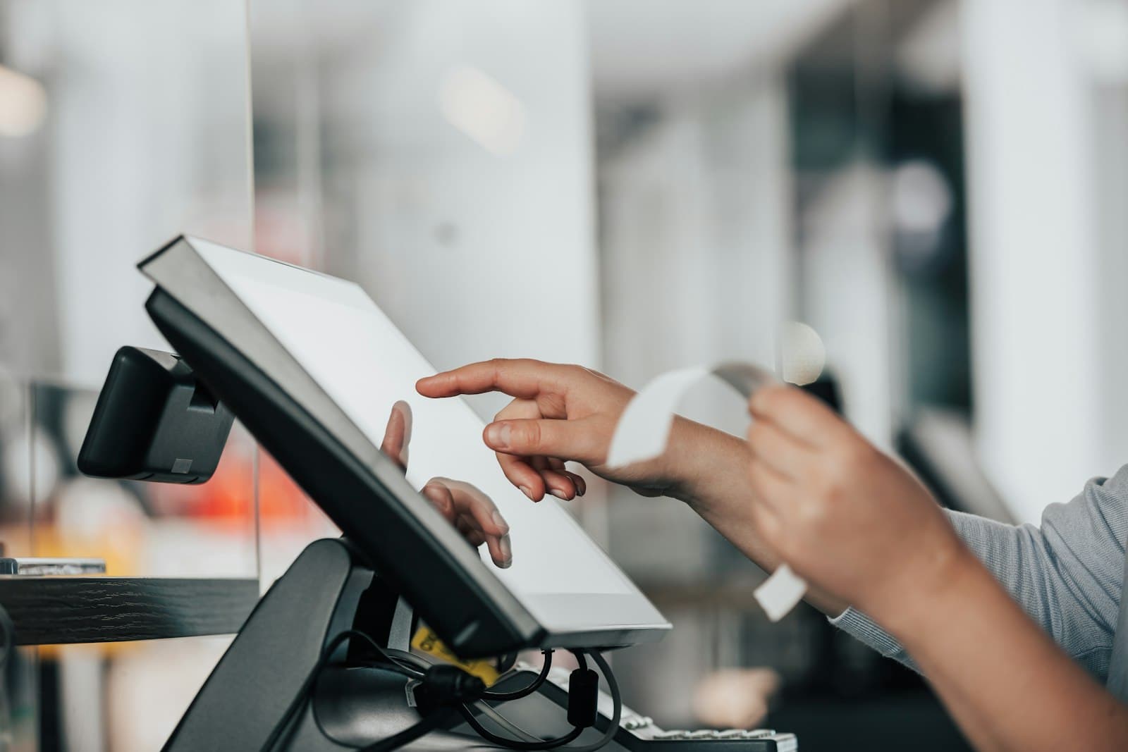 Una mano toca la pantalla de un terminal de punto de venta mientras sale un recibo